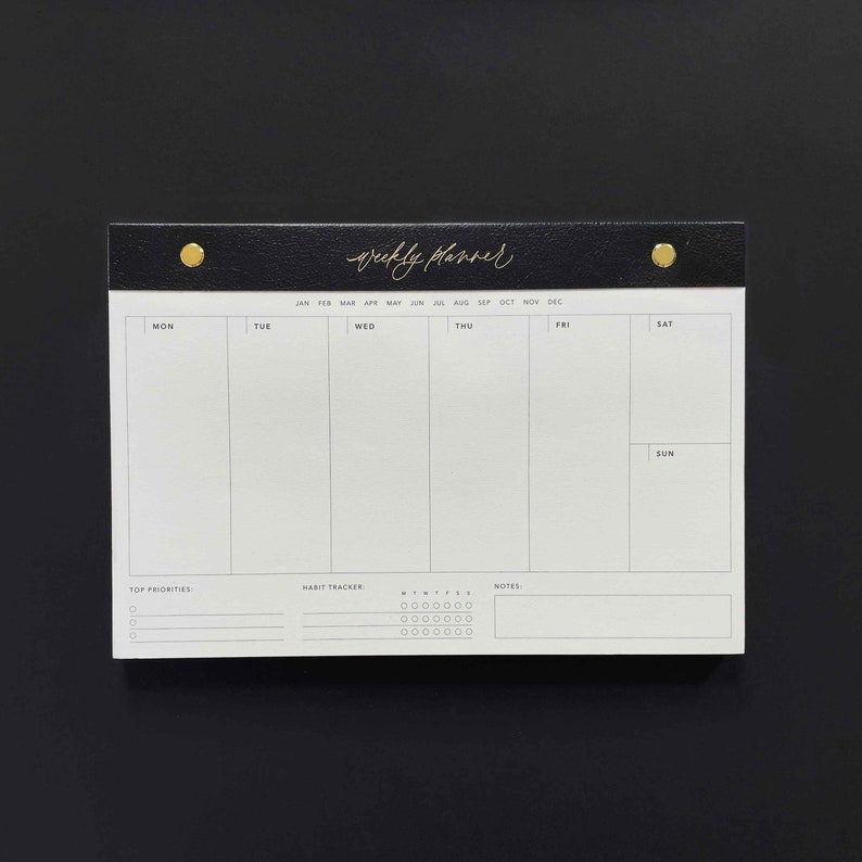 K&ouml;nnte beinhalten: Ein schwarz-wei&szlig;er Wochenplaner mit goldenen Akzenten. Der obere Teil des Planers ist schwarz mit dem goldfarbenen Schriftzug "weekly planner". Er hat Abschnitte f&uuml;r jeden Wochentag, Top-Priorit&auml;ten, einen Gewohnheitstracker und Notizen.