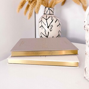 May include: Two stacked notebooks with gold trim. The top notebook is grey and has the word "GROW" embossed in gold on the cover. The bottom notebook is white.