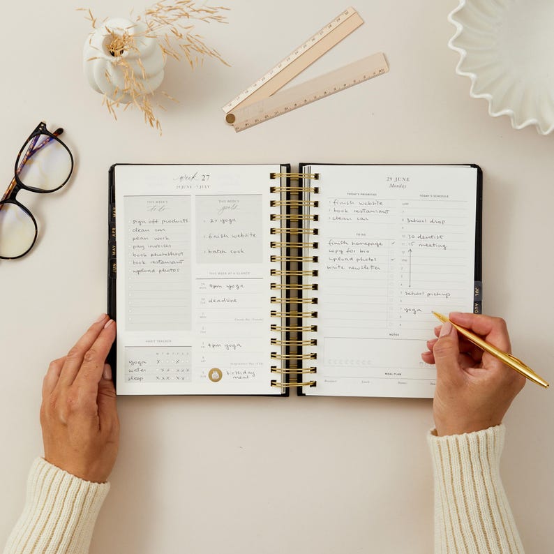 2026 daily planner black vegan leather with gold foiled stickers, tabs, and removable bookmark for organisation.