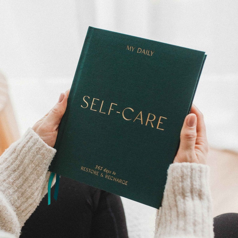 Puede incluir: Un diario verde oscuro con letras doradas que dicen "My Daily Self-Care 365 days to Restore & Recharge".