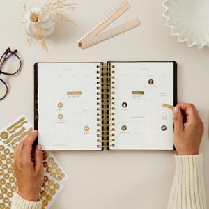 Black 2026 ring-bound daily planner with gold accents, day-to-page diary for appointments, schedules, and goals.