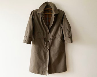 May include: A long, brown, belted trench coat with a plaid lining. The coat has a drawstring waist and button closure.