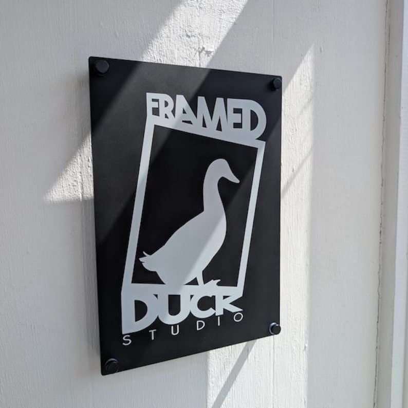 matte black custom acrylic business logo sign, printed with white UV ink. Mounted to the wall of a studio entrace with black standoff fixings.