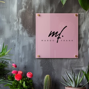 May include: A pink square sign with rounded corners and gold accents. The sign has black text that reads "mf. MARGO FRANK".