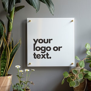 Könnte beinhalten: Ein weißes Acrylschild mit abgerundeten Ecken und goldenen Schrauben. Das Schild trägt den Text "your logo or text." in schwarzer Schrift.
