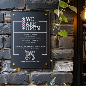 Op de afbeelding: Zwart bord met witte tekst die "We Are Open" luidt. Het bord bevat ook een afbeelding van een barbierpaal, openingstijden en een QR-code. De tekst onderaan het bord luidt "WWW.SPARTANFAB21.COM".
