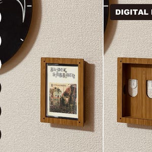 May include: A wooden frame with a clear plastic insert for displaying a record album. The album cover features a black and white image of a house with trees and the text "Black Sabbath". The frame is mounted on a light beige wall. The text "DIGITAL FILE" is visible in the upper right corner of the image.