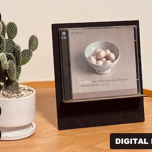 May include: A black CD display stand with a CD featuring a white bowl of eggs on a white background. The text on the CD reads "J.S. Bach Das Wohltemperierte Klavier II Masaaki Suzuki Harpsichord".