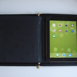 May include: A black leather case with a zipper closure, designed to hold a tablet. The case has a honeycomb pattern on the front and a tablet with a green screen is visible inside.