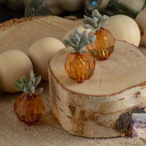 May include: Three small amber glass vases with faux succulents on a wooden slice. The vases are faceted and have a geometric shape. The succulents are a light green colour.