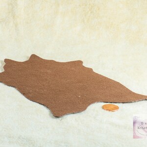 Shows the back side of a miniature cowskin rug. The fabric on the back is a brown canvas style texture. It is on a biege background. It has a penny in front of the rug to show scale.
They are made for 1:12 scale or 1:6 scale miniature dollhouses or diorama scenes and are not full sized.