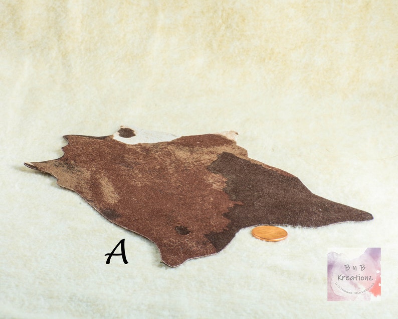 Shows a miniature cowskin rug in shades of brown and white. The rug is irregularly shaped, with a textured appearance. The letter "A" is printed near the rug. The rug is a dollhouse miniature. It is on a biege background with a penny to show scale.
They are made for 1:12 scale or 1:6 scale miniature dollhouses or diorama scenes and are not full sized.