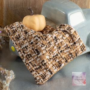 May include: A brown and white patterned fabric blanket with a small, yellow pumpkin on top. The blanket is draped over a toy truck.