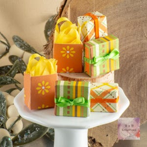 May include: A collection of miniature gift boxes and bags. The boxes are orange with white flower designs and filled with yellow tissue paper. The gift boxes are wrapped in patterned paper with ribbons in green and orange.