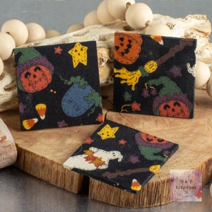 May include: Three black fabric squares with different Halloween-themed patterns. One square features a ghost, another has a witch's broom and a pumpkin, and the third has a pumpkin and a tombstone.