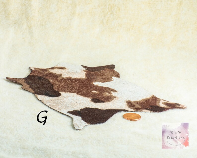 Shows a miniature cowskin style rug in browns and cream. It is on a biege background. The letter G is to the side of the rug. A penny is in front of the rug to show scale.
They are made for 1:12 scale or 1:6 scale miniature dollhouses or diorama scenes and are not full sized.