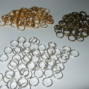 Può includere: Un grande mucchio di anelli di salto argentati, un mucchio più piccolo di anelli di salto dorati e un mucchio di anelli di salto in bronzo. Questi sono anelli metallici utilizzati per la creazione di gioielli.