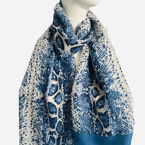 May include: A blue and white snakeskin patterned scarf with a teal border. The scarf is made of a soft, lightweight fabric and is perfect for adding a touch of style to any outfit.