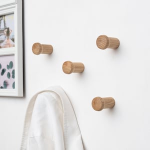 May include: Four wooden wall hooks mounted on a white wall. A white shirt is hanging on one of the hooks.