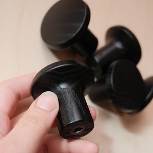 May include: Five black wooden knobs with a round top and a cylindrical base. The knobs have a wood grain pattern and a screw hole in the bottom.