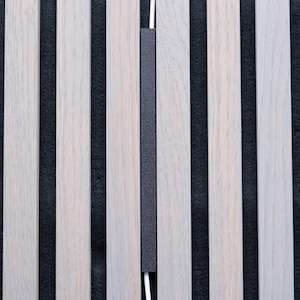 May include: A close-up shot of a wooden panel design with vertical, light-coloured wooden slats and a dark grey accent. A thin, white cable runs vertically through the centre, adding a modern touch. The background is a dark grey, textured surface.