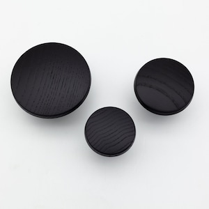 May include: Three black wooden wall hooks of different sizes. The hooks are round and have a wood grain pattern.