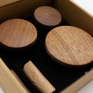 May include: Four round wooden knobs in a cardboard box with black foam padding. The knobs are made of dark brown wood with a natural grain pattern.