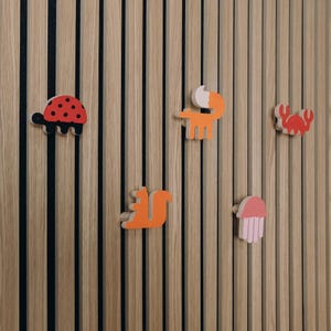 May include: A wooden wall with black vertical lines features five colourful wooden animal cutouts: a ladybug, a fox, a crab, a squirrel, and a jellyfish.