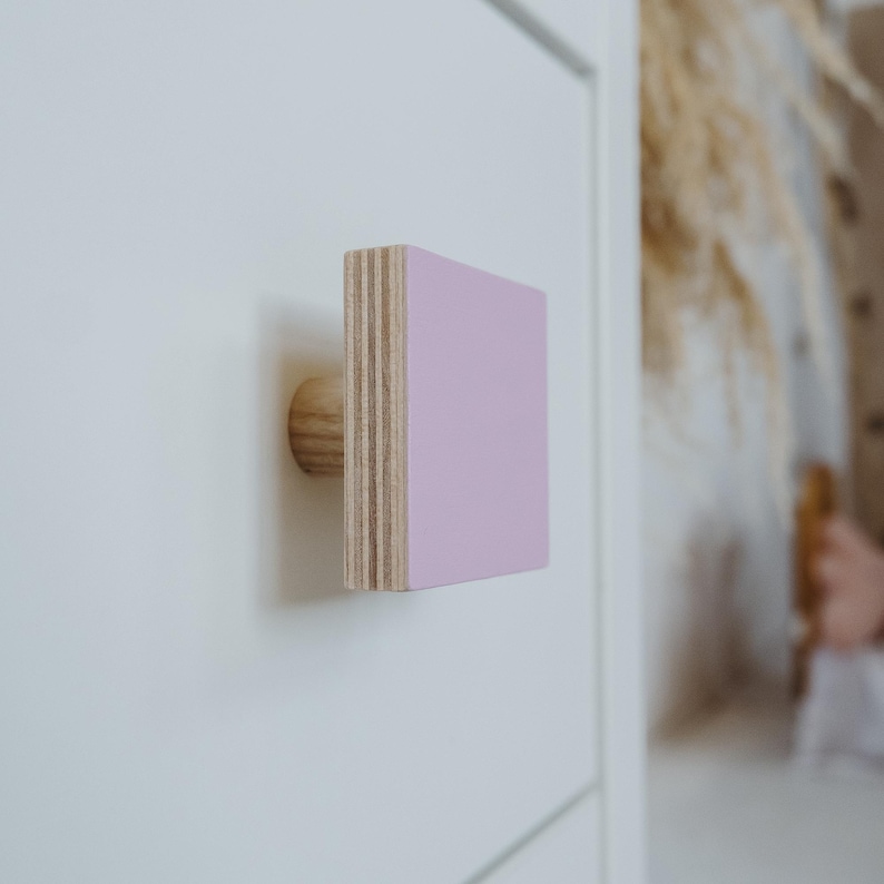 May include: A light pink square cabinet knob with a wooden base.