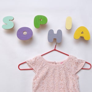 A kids room in the design of which are used multi-colored wooden wall hooks. Wooden Hooks in the form of letters are fixed on the wall and folded in the name of the child for children's clothes.