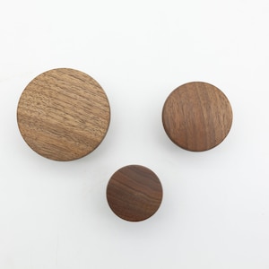 May include: Three round wooden wall hooks in different sizes. The hooks are made of dark brown wood with a natural grain pattern.