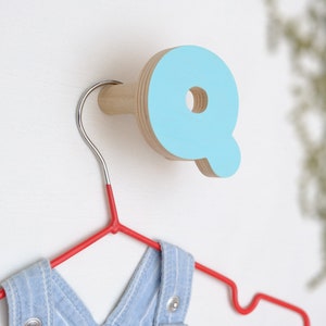 May include: A light blue wooden letter Q wall hook with a red hanger and a blue and white striped onesie hanging on it.