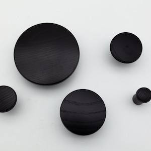 May include: Five black wooden wall hooks of varying sizes. The hooks are round and have a smooth, polished finish.