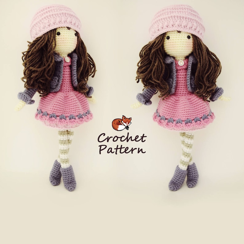 以下が含まれることがあります： ピンクとパープルの髪の毛の茶色のドールのためのクロシェパターン。ピンクのドレス、パープルのジャケット、ストライプのタイツを着用しています。ドールは小さなキツネのぬいぐるみを持っています。