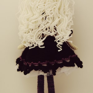 May include: A crocheted doll with long white yarn hair, a black dress with a white lace trim, purple legs, and black shoes.