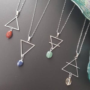 Puede incluir: Collares plateados con colgantes triangulares geométricos y detalles de piedras preciosas de colores. Los collares presentan una delicada cadena y se exhiben sobre un fondo oscuro. Cada colgante tiene una piedra de diferente color.
