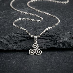 May include: A silver-toned metal pendant featuring a triskelion design with three interconnected spirals. The pendant is suspended from a matching silver-toned metal chain link necklace, showcasing a polished finish and a classic link structure.