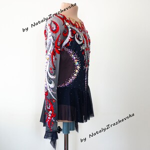 May include: A black and red figure skating dress with intricate rhinestone and sequin embellishments. The long-sleeved dress features a sheer mesh overlay on the sleeves and upper bodice, with a flared skirt. The design includes a crescent of rhinestones on the front.