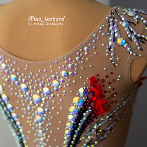 May include: A tan leotard with intricate embellishments, including iridescent rhinestones and red floral accents. Black and silver painted details create a striking contrast. The text "@leo_leotard by Nataly Zrazhevsk" is visible.