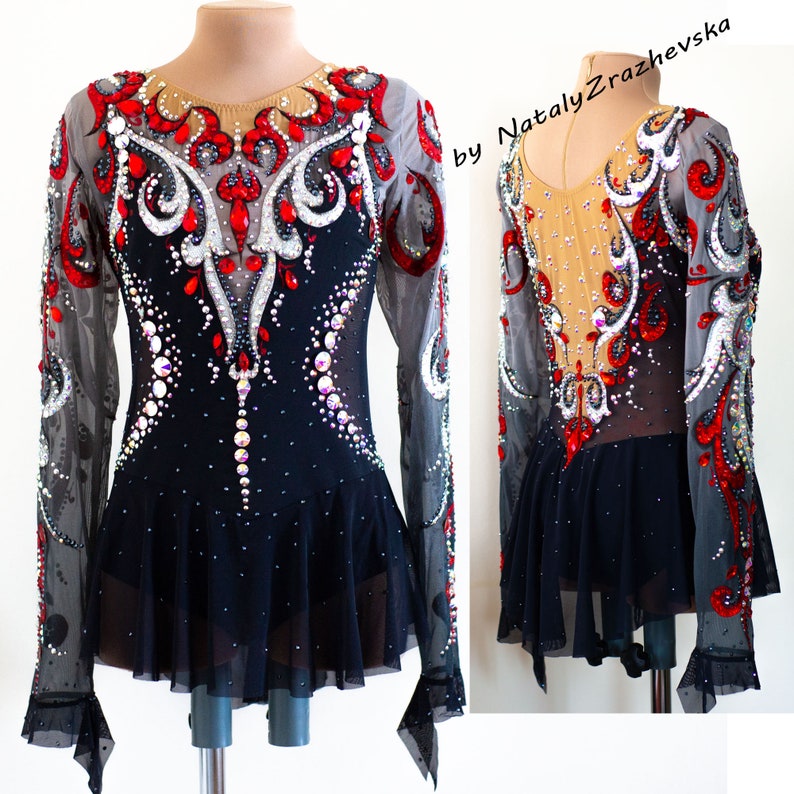 May include: A black and red figure skating dress with long sleeves, embellished with rhinestones and decorative patterns. The dress features a sheer neckline and sleeves, with a flared skirt. The design includes a combination of red, white, and clear crystals.