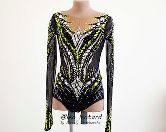 May include: Black long-sleeved leotard with a sheer neckline and sleeves. The leotard is embellished with yellow and clear rhinestones in a decorative pattern. The text "@leo_leotard by Nataly Zrzhevsk" is visible.