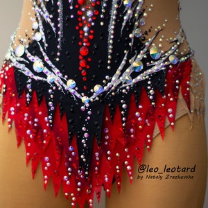 May include: A close-up of a black and red leotard with intricate rhinestone and sequin detailing. The leotard features a high neckline and is embellished with a variety of iridescent and red rhinestones. The design includes a jagged red skirt.