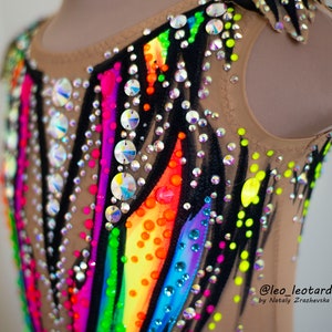 Pu&ograve; includere: Un body color carne con un design a arcobaleno e accenti neri. Il body &egrave; decorato con strass e ha una scollatura rotonda. Il testo "@leo_leotard by Natali  Zrazhevksa" &egrave; stampato nell'angolo in basso a destra del body.