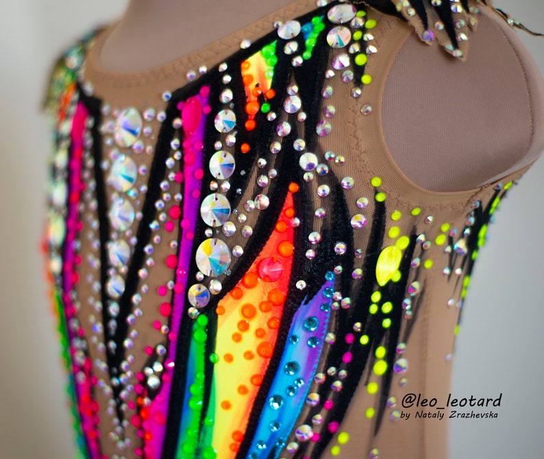 Pu&ograve; includere: Un body color carne con un design a arcobaleno e accenti neri. Il body &egrave; decorato con strass e ha una scollatura rotonda. Il testo "@leo_leotard by Natali  Zrazhevksa" &egrave; stampato nell'angolo in basso a destra del body.