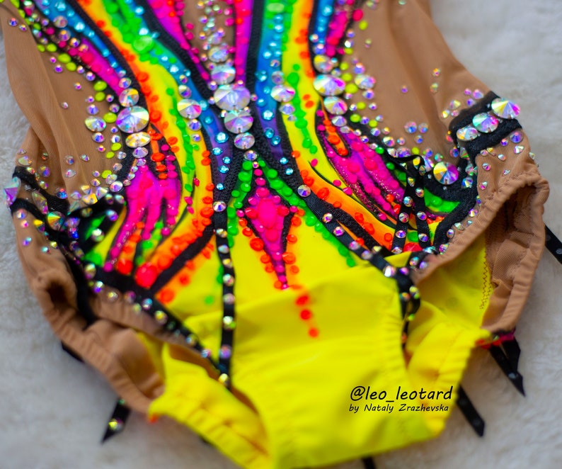Pu&ograve; includere: Un body giallo con un design arcobaleno e accenti neri. Il body &egrave; decorato con strass e ha un'overlay in rete. Il body &egrave; realizzato da @leo_leotard di Natay Zrazhevska.