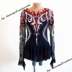 May include: A black and red figure skating dress with long sheer sleeves. The bodice is embellished with red and white rhinestones and a decorative pattern. The skirt is short and flared. The text "by Nataly Zrazhevska" is visible.