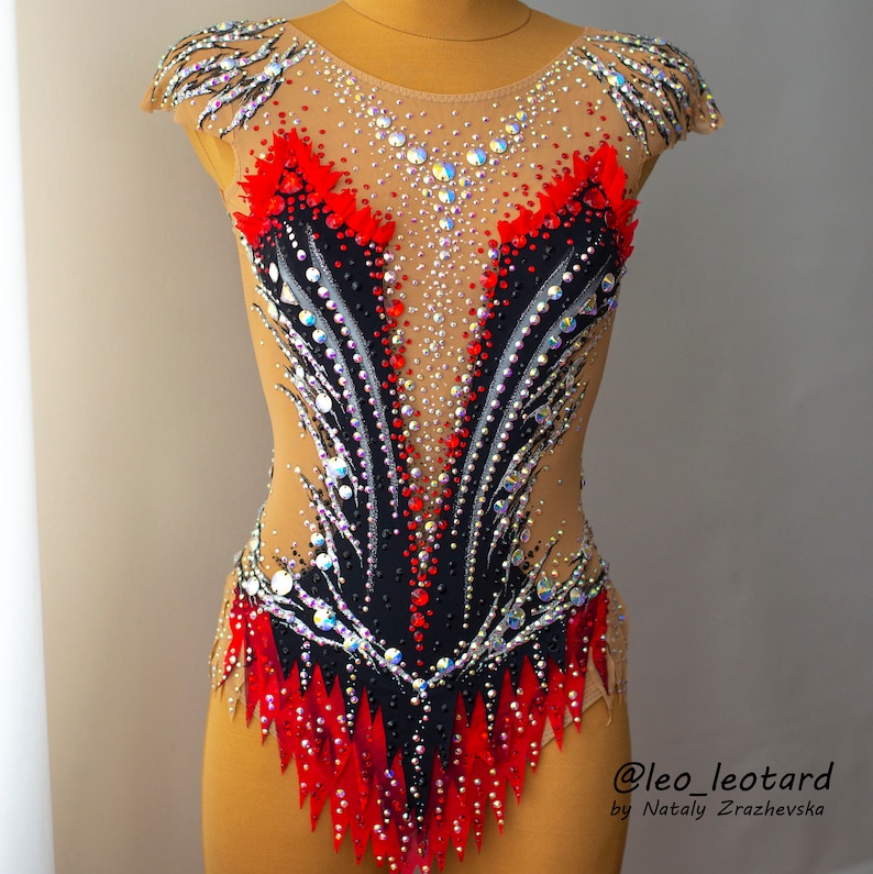 May include: A decorative leotard with a nude base, featuring a striking design of red, black, and silver accents. The leotard is embellished with numerous sparkling rhinestones, creating a dazzling effect. The design is symmetrical and intricate.