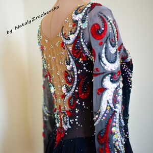 May include: A long-sleeved leotard with intricate embellishments. The garment features a sheer nude mesh back and sleeves, adorned with red, silver, and clear crystals. The design includes swirling patterns and a black skirt. The text "by Nataly Zrazhevska" is visible.