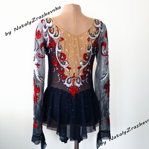 May include: A figure skating dress with long sleeves. The bodice is beige with intricate red, black, and silver embellishments. The sleeves are sheer gray, and the skirt is navy blue with a ruffled hem. The text "by Nataly Zrazhevska" is visible.