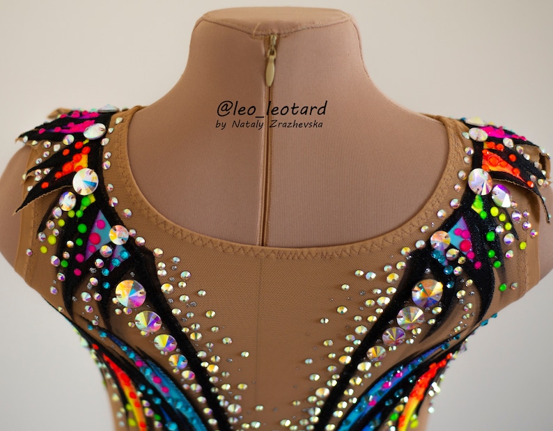 Pu&ograve; includere: Un body color carne con un design a arcobaleno e accenti neri. Il body &egrave; decorato con strass e ha una cerniera sul retro. Il testo "@leo_leotard by Nataly  Zrazhevksa" &egrave; stampato sul retro.